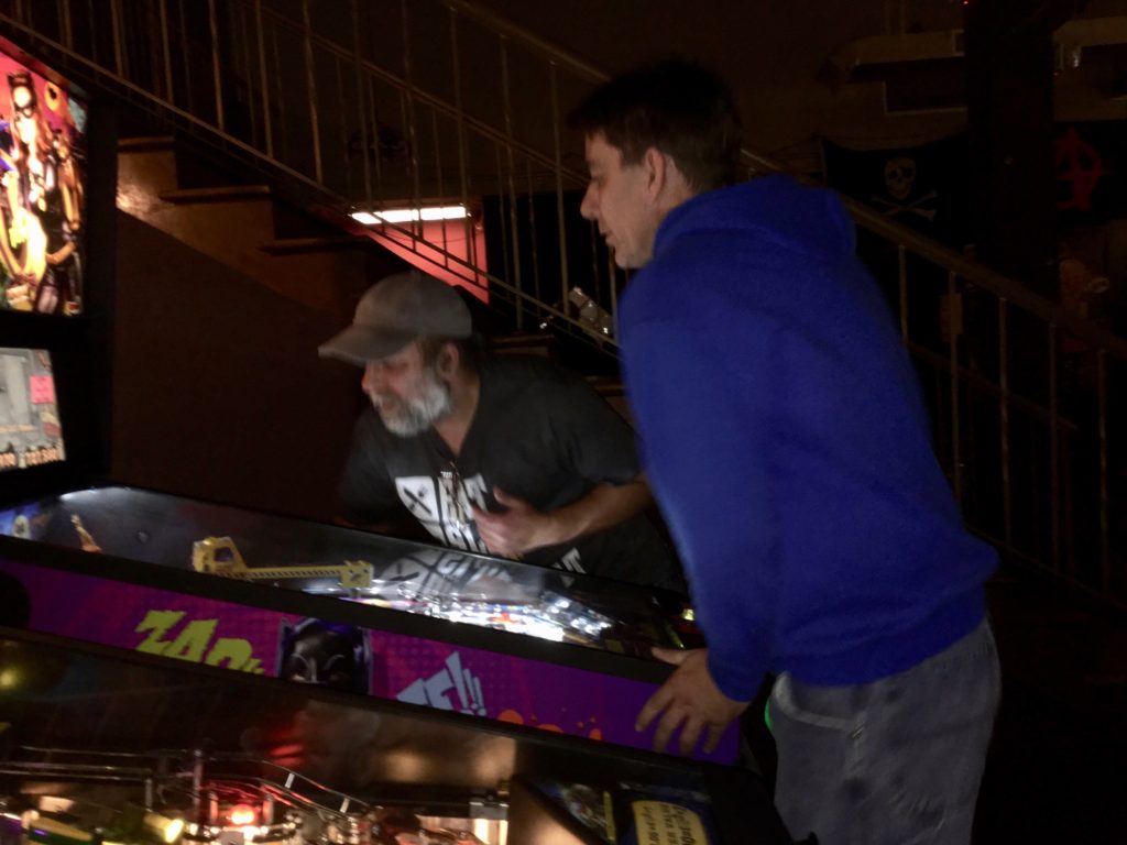 Biff holds the flipper while Pat looks at the upper playfield of a game.